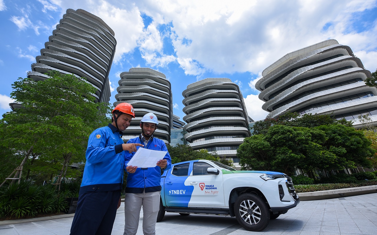 two TNB staff pose in front of TNB building with an EV truck